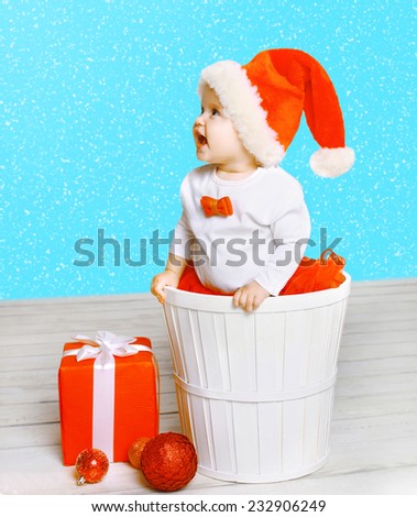 Christmas and people concept - joyful positive child in santa hat with gifts against the snowflakes