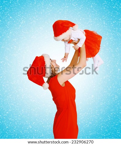Christmas and people concept - happy mother and baby in santa hats having fun against the snowflakes
