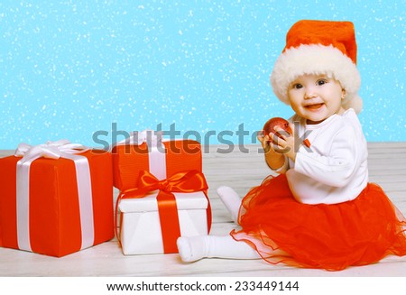 Christmas and people concept - cute smiling baby with gifts against the snowflakes