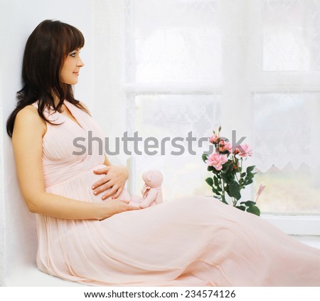Beautiful pregnant woman in dress at home, dreams of a future child looking in window