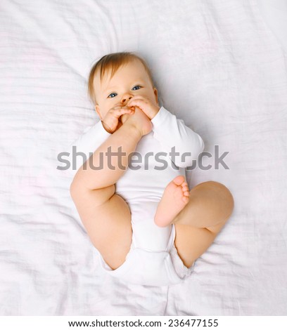 Cute baby lying on the bed takes feet in mouth