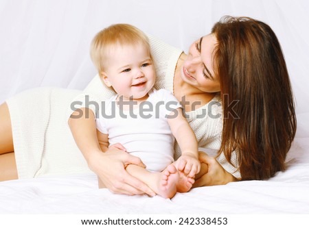 Happy mom and baby having fun in bed at home, life moment