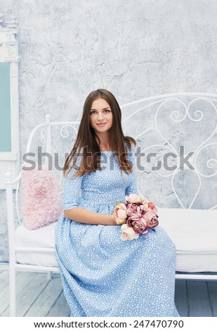 Lovely young woman in the spring dress with flowers in white room