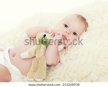 Little baby with teddy bear lying on the bed