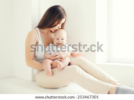 Lovely young mom kissing her baby at home in light room