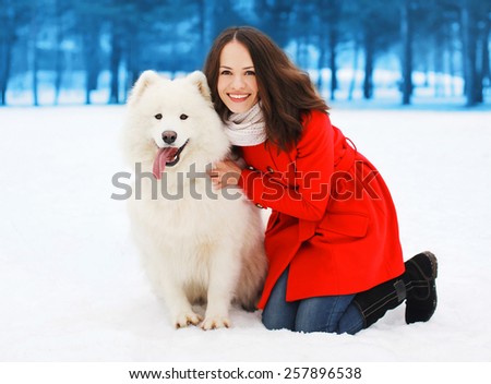 Winter and people concept - happy woman having fun with white Samoyed dog outdoors in winter day