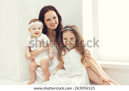 Portrait of happy family, mother together with two children at home in white room near window