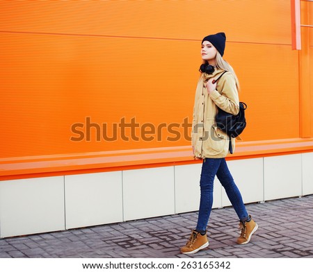 Outdoor fashion photo of stylish hipster cool girl walking in the city against a colorful urban wall