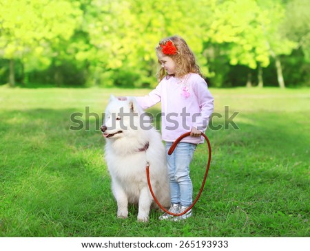 Child with white Samoyed dog on the grass in sunny summer day
