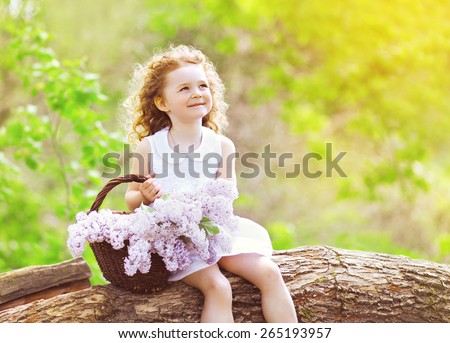 Little girl with basket of lilac flowers sitting and enjoying sunny summer day