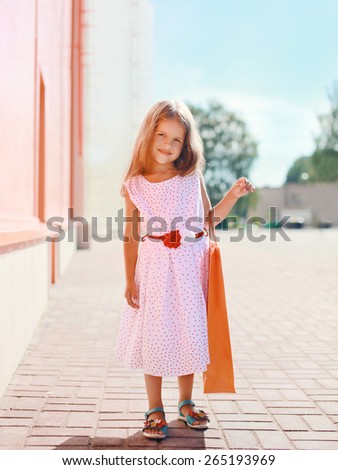 Beautiful little girl in white dress with shopping bag, sunny summer day