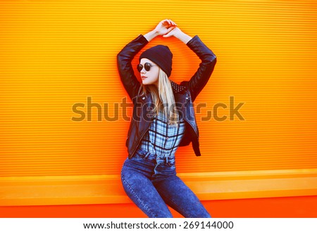 Street fashion concept - stylish cool girl in rock black style posing against a colorful orange urban wall