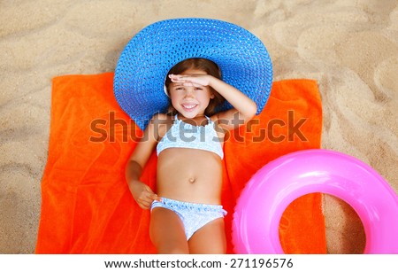 Summer, vacation and people concept - little girl in bikini and straw hat lying sunbathing on the sand beach
