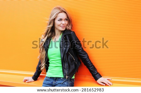 Portrait of beautiful blonde woman wearing a black rock leather jacket against the colorful orange wall, street fashion