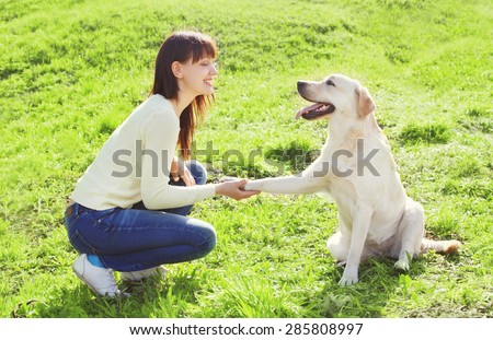 Happy owner woman with labrador retriever dog trains on the grass in summer day