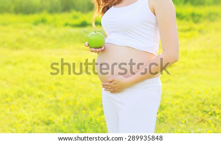 Pregnancy, sport and health lifestyle - young pregnant woman with green apple in sunny summer day