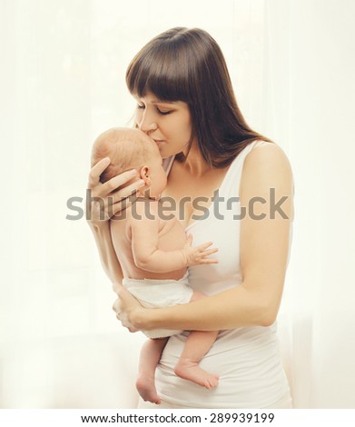 Portrait of loving mom kissing little baby at home