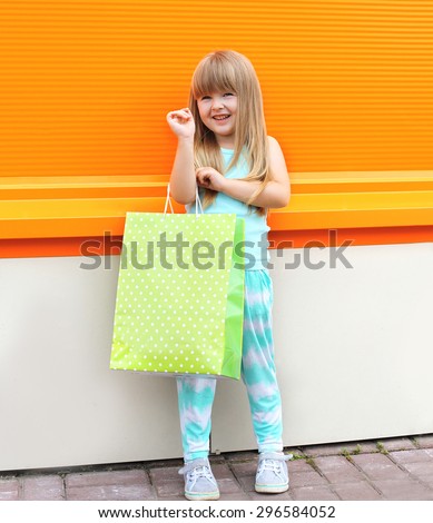 Portrait of beautiful smiling little girl child with shopping bag against the colorful orange wall