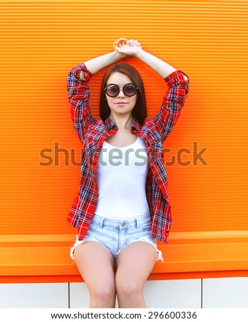 Fashion pretty woman in the sunglasses and checkered shirt posing against the colorful orange wall