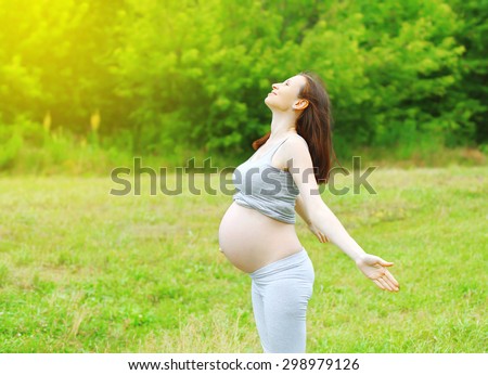 Happy pregnant woman enjoys sunny summer day on the grass