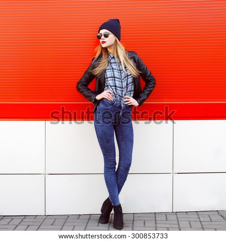 Street fashion concept - pretty young slim woman in rock black style posing against the red wall