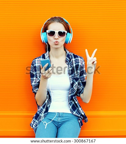 Pretty cool girl having fun and listens to music in the headphones on smartphone over colorful background