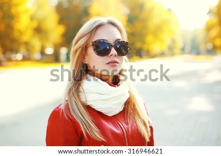 Portrait of fashion blonde woman wearing a sunglasses and red leather jacket with scarf in autumn park
