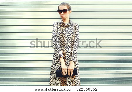 Fashion pretty young woman in sunglasses and leopard dress with handbag clutch over metal background