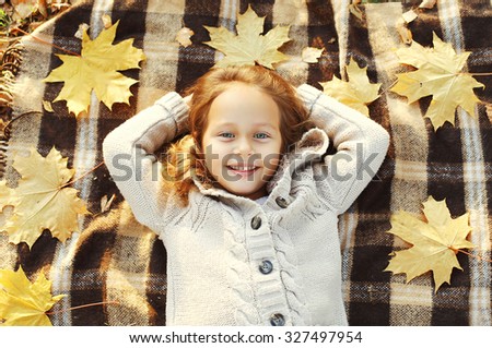 Portrait happy smiling child lying on plaid with yellow maple leafs in autumn day