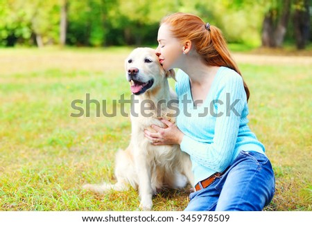 Happy owner woman kissing Golden Retriever dog on grass