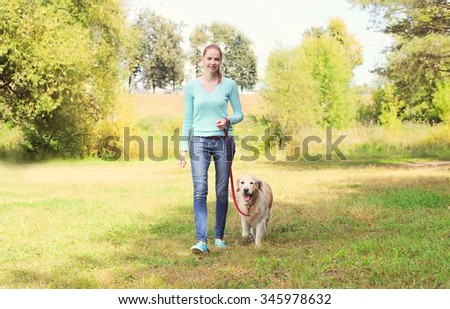 happy owner woman and Golden Retriever dog walking together in summer park