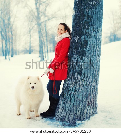 Happy smiling young woman owner with white Samoyed dog walking in winter park