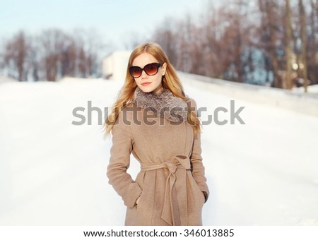 Beautiful elegant blonde woman wearing a coat jacket and sunglasses in winter city