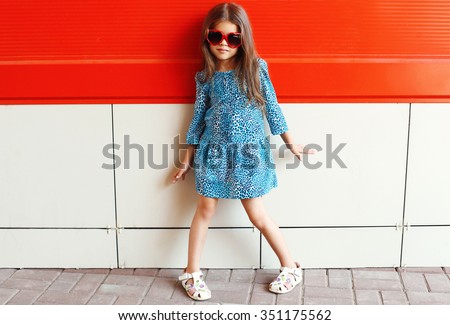 Beautiful little girl model wearing a leopard dress and sunglasses over colorful red background