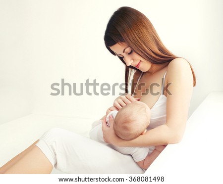 Young mother feeding breast her baby at home in white room