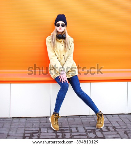 Fashion pretty blonde girl in city over colorful orange background