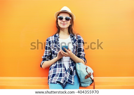 Pretty smiling woman using smartphone in city over orange background