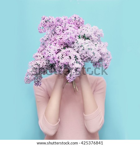 Woman hiding head in bouquet lilac flowers over colorful blue background