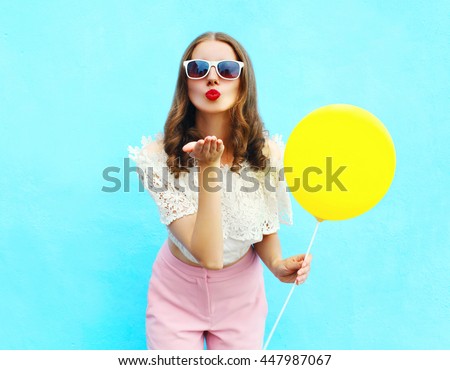 Pretty woman in sunglasses with air balloon sends an air kiss over colorful blue background