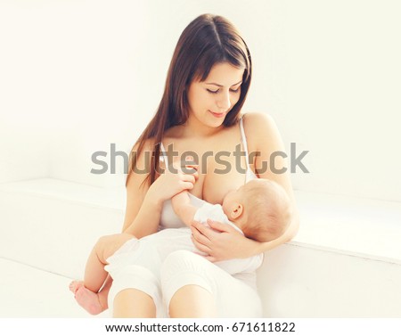 Happy young mother feeding breast her baby at home in white room