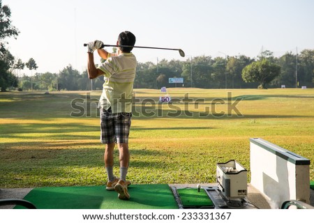 A man swinging club at a driving range.