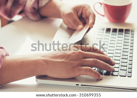 Man\'s hands holding a credit card and using pc or laptop for online shopping