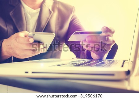 Man\'s hands holding a credit card and using smart phone for online shopping,retro effect.