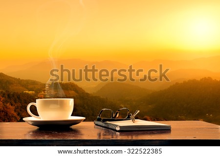 cup of coffee ,notebook and glasses with mountain at morning sunrise.