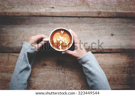 A female hands holding cup of coffee latte art on wood table. above view and vintage effect.