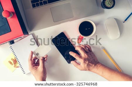 man\'s hands holding a credit card and using smart phone for online shopping.Vintage or retro color effect.