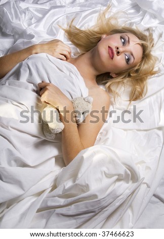 Girl with plush toy in bed wrapped in white sheets