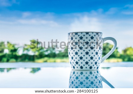 A cup of coffee on white table near the river and tree background