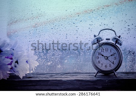 Retro alarm clock on table.10.10 am and rainy day window background,vintage cement texture style