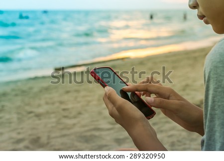 Asian woman holding mobile (red case) on the beach background